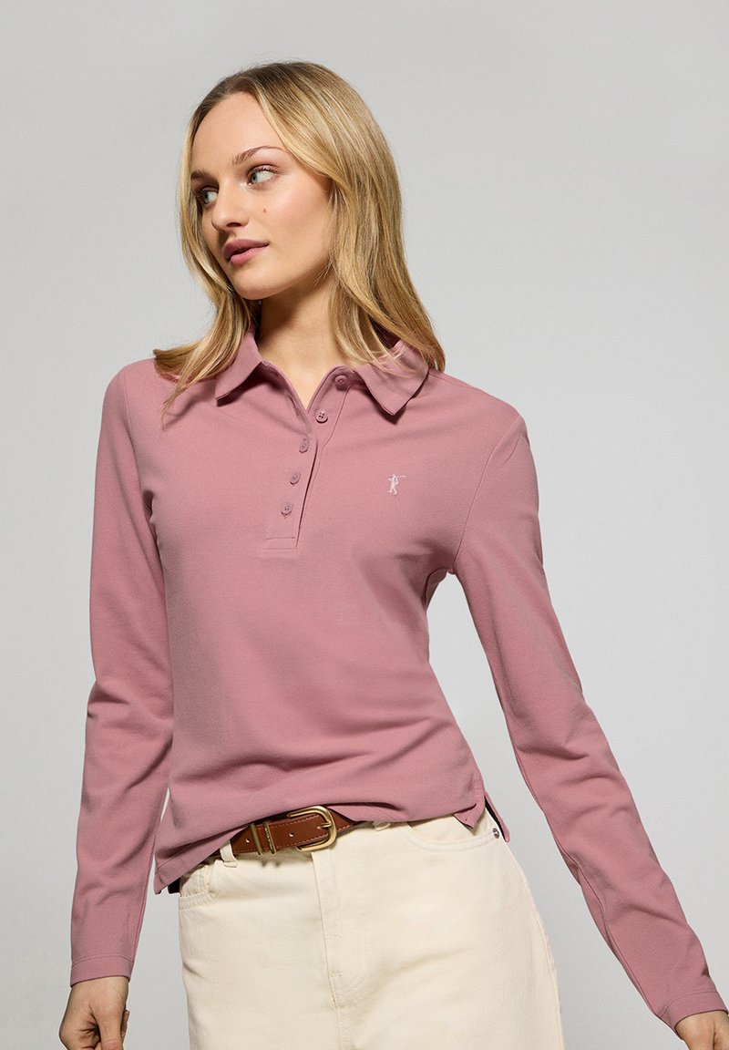 Långärmad polo i ljusrosa, tillverkad av bomull, med en knappslå och sidoslitsar. Liten logotyp på vänster bröst.