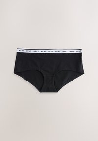 Culottes hipster noires pour femmes avec une ceinture élastique blanche répétant le mot "NEXT" en texte noir, posées à plat sur un fond beige.