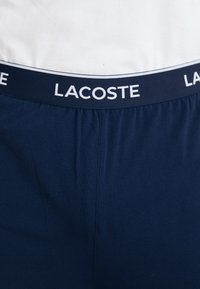 Shorts de marină cu talie elastică, prezentând un logo alb "LACOSTE". Textură netedă cu un design ajustat.