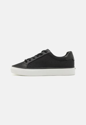 Czarny niski sneaker z subtelnym wzorem logo, czarnymi sznurówkami i grubą białą gumową podeszwą, przedstawiony na białym tle z boku.