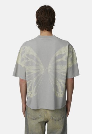 T-shirt grigia a maniche corte con un grande design a forma di ala di farfalla sul retro, caratterizzato da un motivo a puntini giallo chiaro. Realizzata in cotone con una vestibilità comoda.