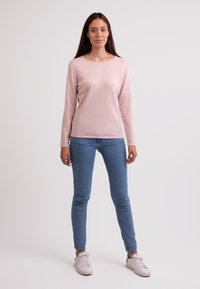 Jasnoróżowy sweter z długim rękawem i okrągłym dekoltem, w połączeniu z dopasowanymi niebieskimi dżinsami i białymi trampkami. Prosty i schludny design.