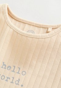 Tissu côtelé beige en gros plan montrant un col arrondi et un texte partiel gris "hello world." imprimé sur le matériau.