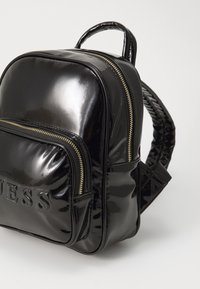 Sac à dos en cuir verni noir avec une finition texturée, comportant une poche zippée à l'avant et des accents en métal doré. Double bretelles.
