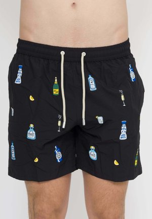 Costume da bagno nero con coulisse bianche con motivi colorati di bottiglie e bicchieri indossato da una persona.