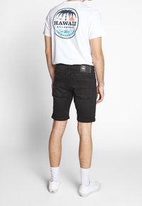 Černé denimové šortky s ohrnutými lemy, které jsou spárovány s bílým tričkem s barevným kruhovým grafickým potiskem na zadní straně. Bílá obuv dokončuje vzhled.