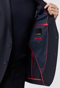 Marineblaues Sakko mit rotem Futter. Im Inneren befindet sich ein Etikett mit "Roy Robson" sowie Symbole für "Slim Fit" und "Stretch". Glatte Textur.