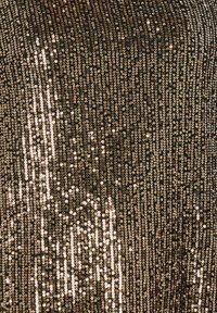 Tela negra adornada con filas verticales de lentejuelas doradas, creando una textura brillante. Las lentejuelas varían en tamaño y reflejan la luz.