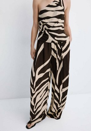 Conjunto de top de un hombro y pantalones de pierna ancha con llamativas rayas abstractas de cebra en negro y beige, combinado con sandalias negras de punta abierta.