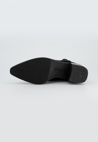 Suela de zapato negra con diseño de punta afilada, superficie de goma texturizada y un sutil logo. El tacón tiene un acabado suave y bordes redondeados.