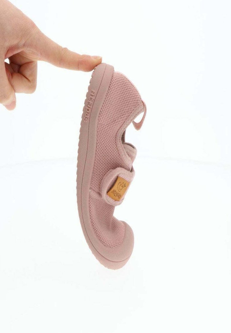 Zapato de punto rosa con una correa de velcro y un acento de cuero marrón claro. Punta redondeada y suela de goma flexible. Parte superior ligeramente texturizada.
