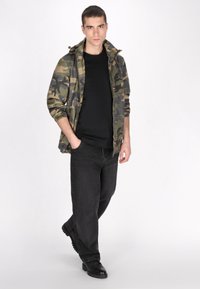 Sateen takki hupulla, musta t-paita ja väljät mustat farkut, yhdistettynä mustiin saappaisiin. Yksinkertainen muotoilu neutraaleilla väreillä.