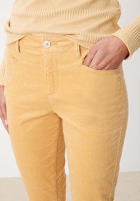 Pantaloni in corduroy giallo con vestibilità slim, dotati di chiusura frontale con bottone, tasche laterali e superficie morbida al tatto.