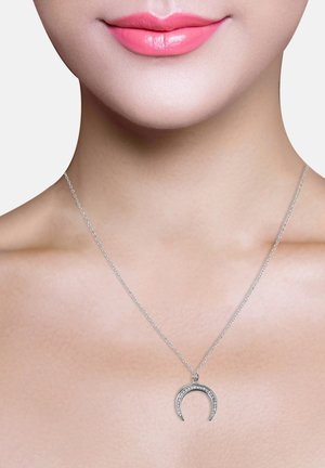 Silberne Halskette mit einem halbmondförmigen Anhänger, der mit kleinen klaren Steinen verziert ist, und an einer feinen Kette vor einem neutralen Hintergrund hängt.