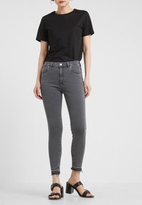 Camiseta negra de manga corta combinada con jeans grises de cintura alta, con un corte ajustado y dobladillo deshilachado, llevada con sandalias negras de tacón cuadrado.
