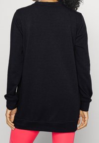 Sweat-shirt noir à manches longues, col et ourlet côtelés. Texture douce, vue arrière montrant une coupe décontractée, porté sur des leggings rose.