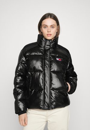 Chaqueta acolchada negra con cuello alto, acabado brillante, bolsillos laterales y puños acanalados. Presenta un pequeño parche de logo en el lado izquierdo del pecho.