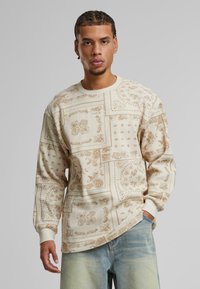 Beige sweatshirt with intricate brown patterns, featuring long sleeves and a rounded neckline, made of textured fabric with subtle accents.