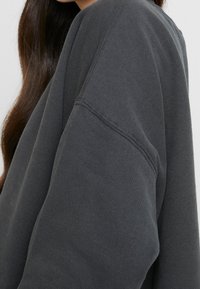 Gray sweatshirt with a loose fit and ribbed cuffs, featuring a textured fabric and dropped shoulder seam detail.