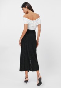 Witte off-shoulder top met gedrapeerde details, gecombineerd met een zwarte kanten maxi rok. Biedt een getailleerde silhouet en subtiele textuur op de stof.