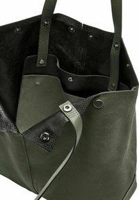 Zielona skórzana torba typu tote z czarnymi zamszowymi akcentami, wieloma wewnętrznymi kieszeniami oraz srebrnymi zapięciami na zatrzask. Teksturowany i sztywny design.
