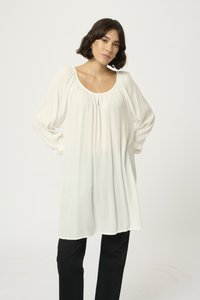Witte, geplooide tuniek met een ronde halslijn, een klein knoopdetail en luchtige lange mouwen, gecombineerd met zwarte broek. Soepele textuur.