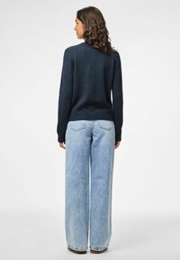 Jūras pārklājs ar garām piedurknēm, vidēja svara. Saskaņots ar gaiši ziliem platajiem džinsiem, kuriem ir klasiskā piecu kabatu dizains.