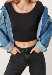 Svart kort topp i kombination med en ljusblå denimjacka. Jackan har stora knappar och en avslappnad passform, med svarta högmidjade jeans.