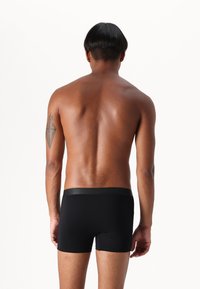 Black boxer briefs made of smooth fabric, featuring a black waistband with subtle branding, shown from the back on a bare torso.