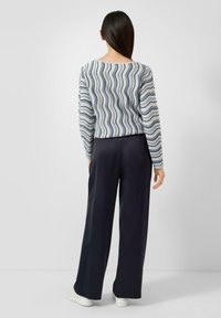 Gestreept top met lange mouwen in blauw en wit met golven, gecombineerd met zwart wijde broekspijpen en witte sneakers. Zachte textuur, losse pasvorm.