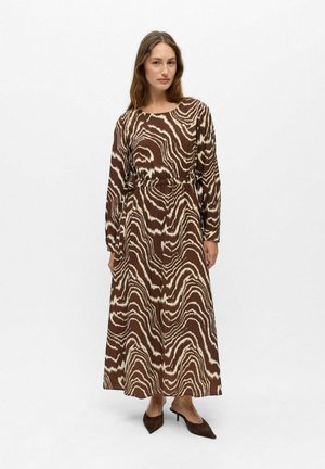 Femme portant une longue robe marron et crème à imprimé zèbre avec manches longues et ceinture, associée à des escarpins marron à bout pointu.