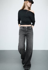 Mustat olkapäiltä avainteet, jotka on yhdistetty väljät, haalistuneet mustat leveälahkeiset farkut. Asusteena on mustat kengät ja yhteensopiva lippis.