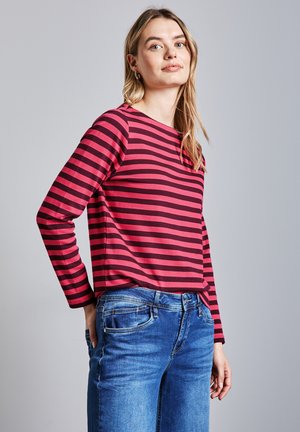 Langarm T-shirt met ronde hals in horizontale strepen in donkerroze en zwart. Gecombineerd met blauwe spijkerbroeken. Glad stofmateriaal.