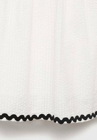 Tessuto bianco texturizzato con motivo a griglia, caratterizzato da un bordo ondulato nero lungo l'orlo. Il design complessivo è semplice ma distintivo.