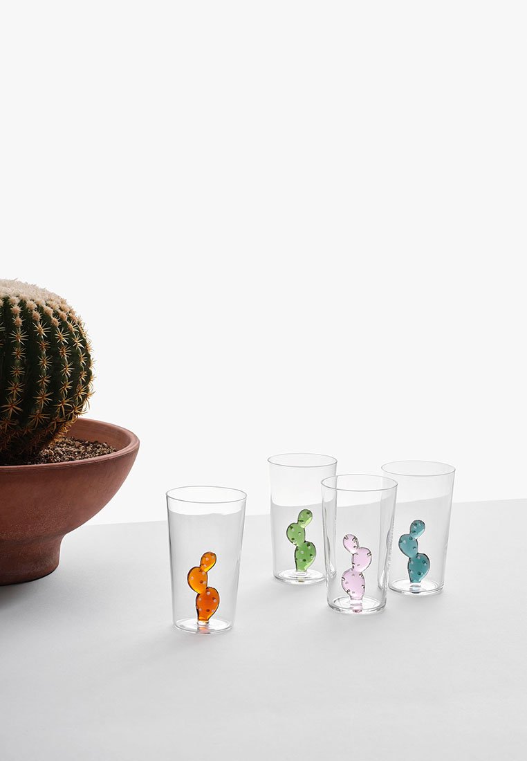 Cztery przezroczyste szklanki z kolorowymi akcentami w kształcie kaktusa: pomarańczowym, zielonym, różowym i niebieskim. W tle znajduje się okrągła doniczka z terakoty z kaktusem.