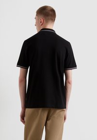 Polo noir à manches courtes, avec des bordures blanches contrastantes sur le col et les bords des manches. Matière en coton, coupe décontractée.