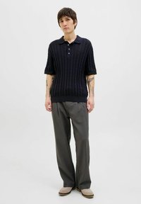 Polo de bumbac tricotat de culoare bleumarin, cu un model texturat, mâneci scurte și guler cu trei nasturi, asortat cu pantaloni gri și încălțăminte bej.