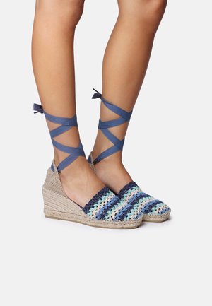 Espadrillas con zeppa e tomaia in tessuto intrecciato, caratterizzate da strisce blu e verde acqua, completate da nastri blu attorno alle caviglie. Suola in juta naturale.