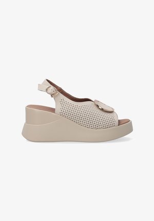 Beżowe perforowane buty na boku z okrągłym czubkiem, na koturnie, z dekoracyjnym okrągłym akcentem na cholewce. Regulowany pasek wokół kostki.