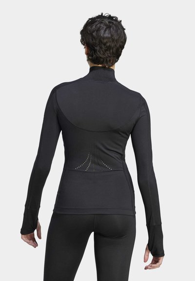 Camiseta atlética negra de manga larga con cuello alto, que presenta detalles con puntos en la parte posterior y agujeros para los pulgares en los puños. Tejido suave y elástico.