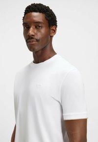 Witte T-shirt met korte mouwen, gemaakt van zachte stof, met een ronde halslijn en een subtiele reliëflogo op de borst, met contrasterende accenten op de mouwen.
