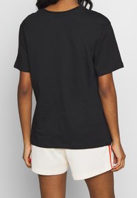 Person iført en ensfarvet sort T-shirt med korte ærmer og hvide shorts med orange lodrette striber, vist fra ryggen.