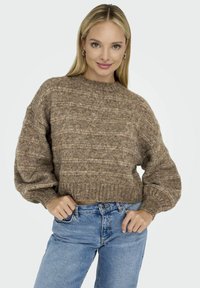 Pull en maille texturée marron avec un col rond et des manches ballons, associé à un jean en denim bleu. Le pull présente des rayures horizontales.
