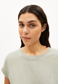 T-shirt in cotone verde chiaro con maniche corte arrotolate, scollatura rotonda e logo ricamato discreto sul davanti. Tessuto morbido, vestibilità casual.