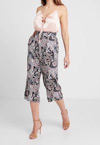 Camisola di raso rosa con dettaglio a lacci, abbinata a culotte nere con motivo paisley e sandali con tacco nudi.