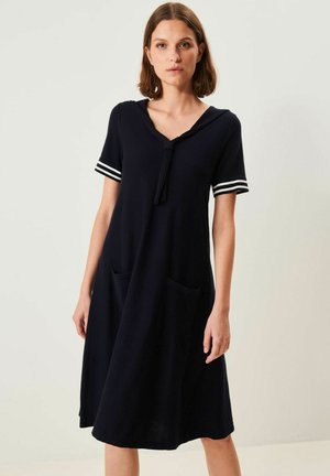 Marineblå knælængde kjole med korte ærmer og hvide stribede detaljer, med V-hals, bindebånd foran og to lommer på forsiden.
