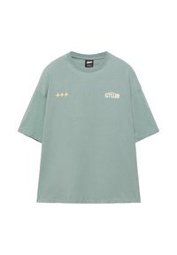 Tricou supradimensionat verde deschis cu mâneci scurte, având trei forme galbene de stea pe pieptul stâng și logo-ul alb "STWD" pe pieptul drept.