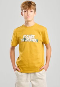 Camiseta de algodón amarilla con gráfico de "ESCAPAR A LA NATURALEZA" que presenta cactus y plantas en colores vibrantes. Mangas cortas y un diseño clásico de cuello redondo.