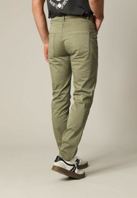 Chinos vert olive avec une coupe ajustée, cinq poches et des détails de couture discrets, associés à des baskets blanches et noires.
