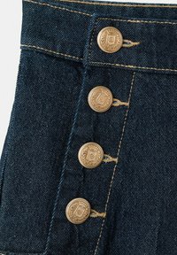 Tmavomodrá rifľová látka so štyrmi zlatými dekoračnými gombíkmi usporiadanými vertikálne pozdĺž prešitých gombíkových dierok.